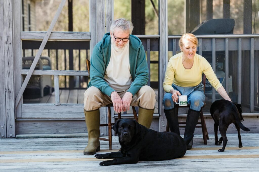 Casal idoso sentado com dois cães na varanda de madeira, desfrutando de momento tranquilo ao ar livre
