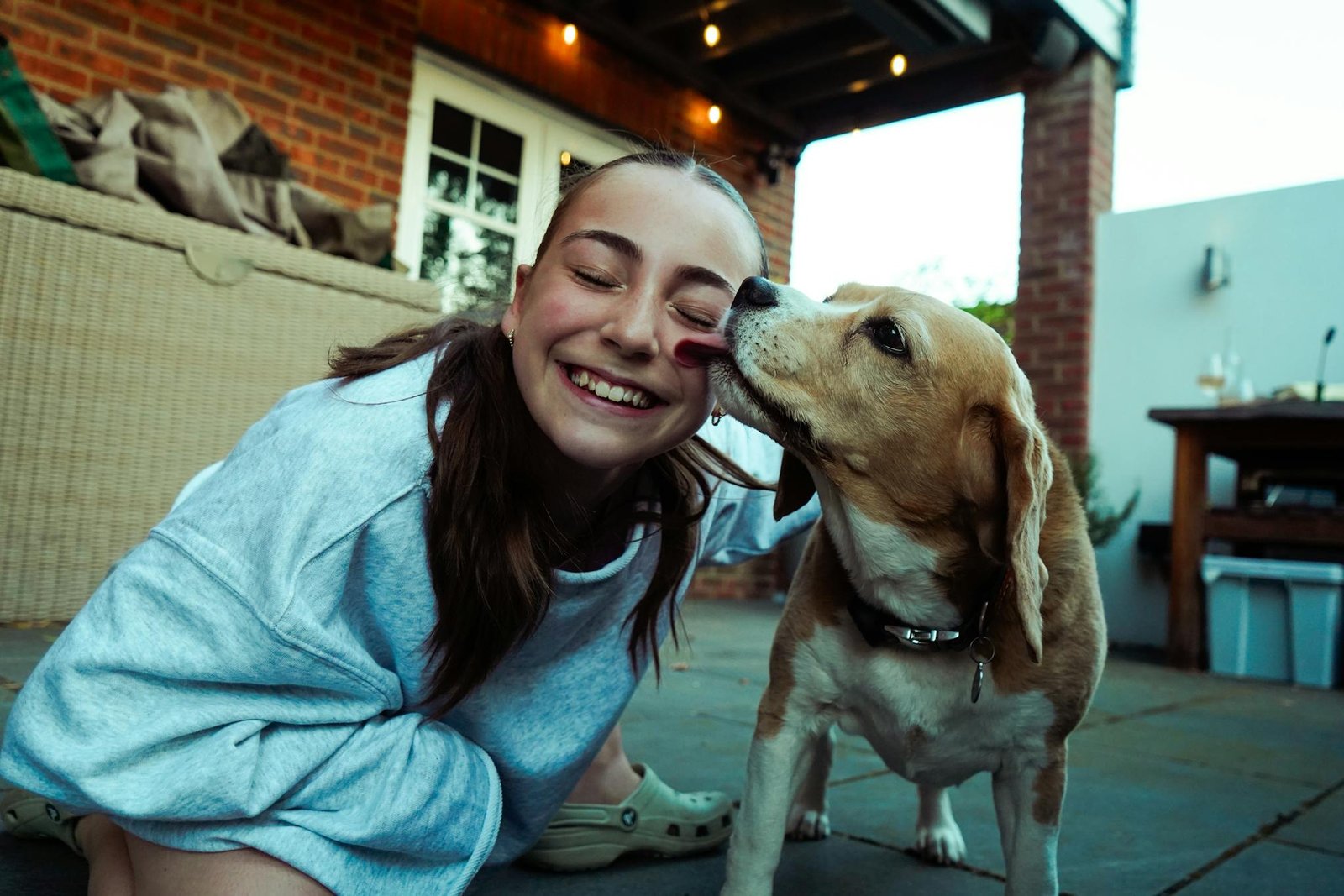 Garota alegre e Beagle compartilhando momento de carinho no pátio, simbolizando felicidade e companheirismo