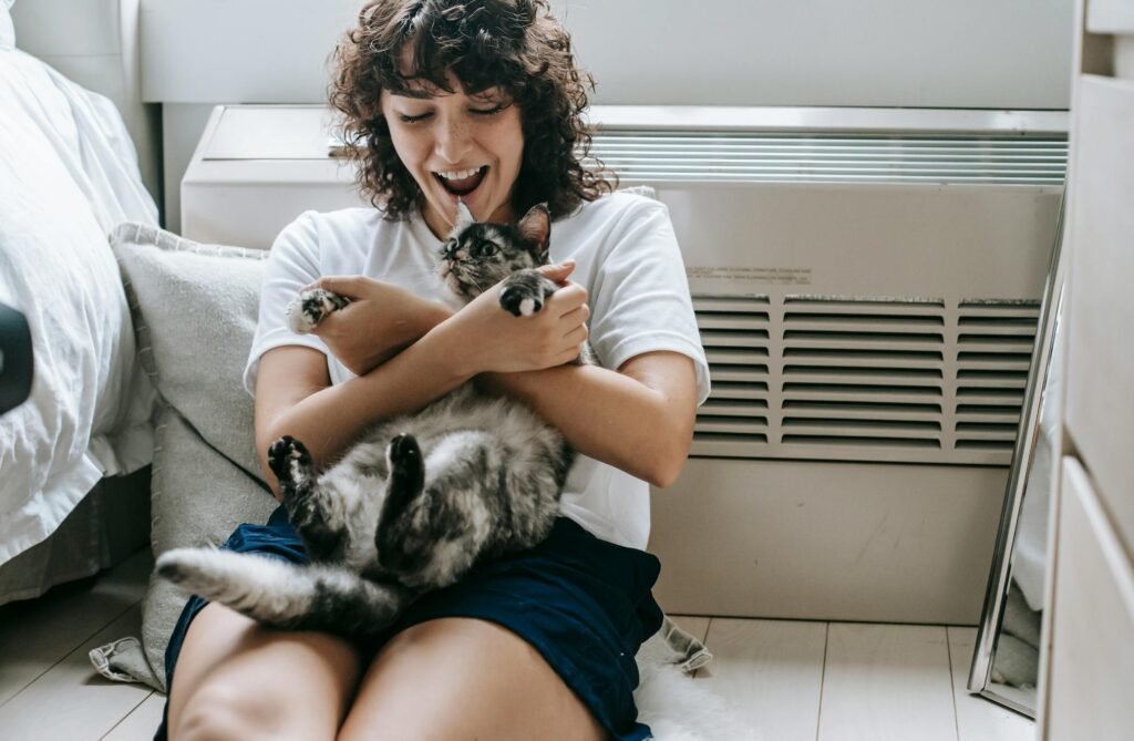 Mulher feliz com cabelos escuros acariciando gato malhado em casa