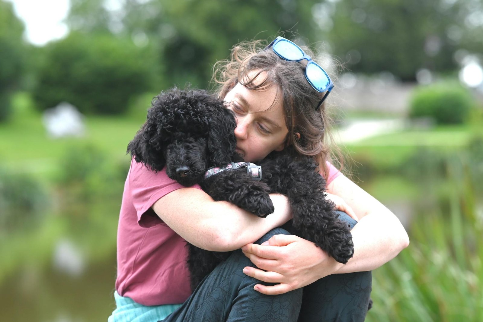 Mulher abraçando um cachorro poodle preto ao lado de um lago tranquilo, transmitindo calor e amizade
